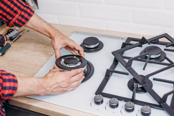 Man hand install burner ongas hob in kithen, close up. Repairs of gas control panel